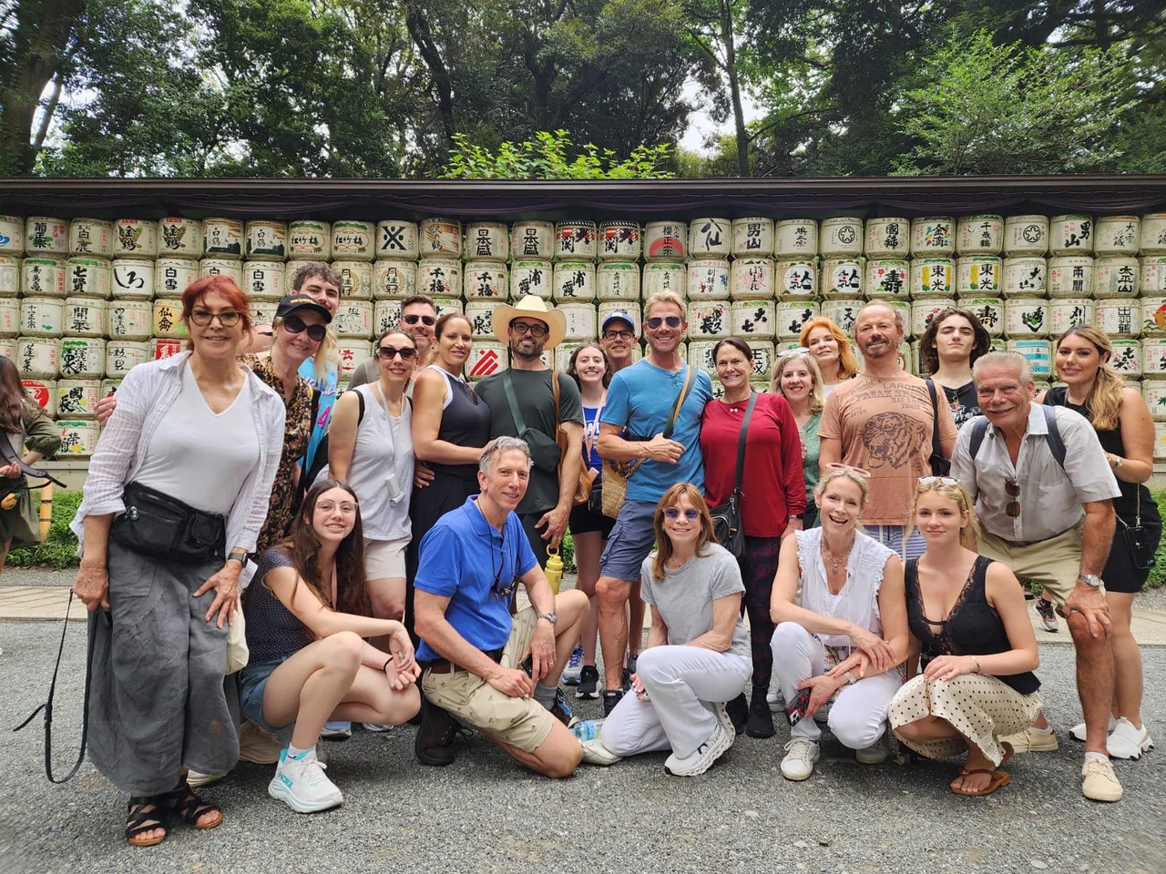 Tour guests posing in front of a wall of decorated sake barrels